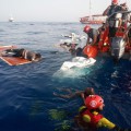 EDITORS NOTE  Graphic content   A member off the Spanish NGO Proactiva Open Arms holds the body of a dead child  R  as other members rescue a woman  C  out off the sea and onto a zodiac rescue boat in the Mediterranean sea about 85 miles off the Libyan coast on July 17  2018    AFP PHOTO   PAU BARRENA